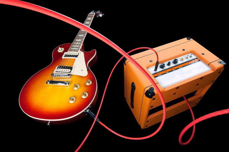 Red audio cable connecting an electric guitar to an orange amplifier against a black background